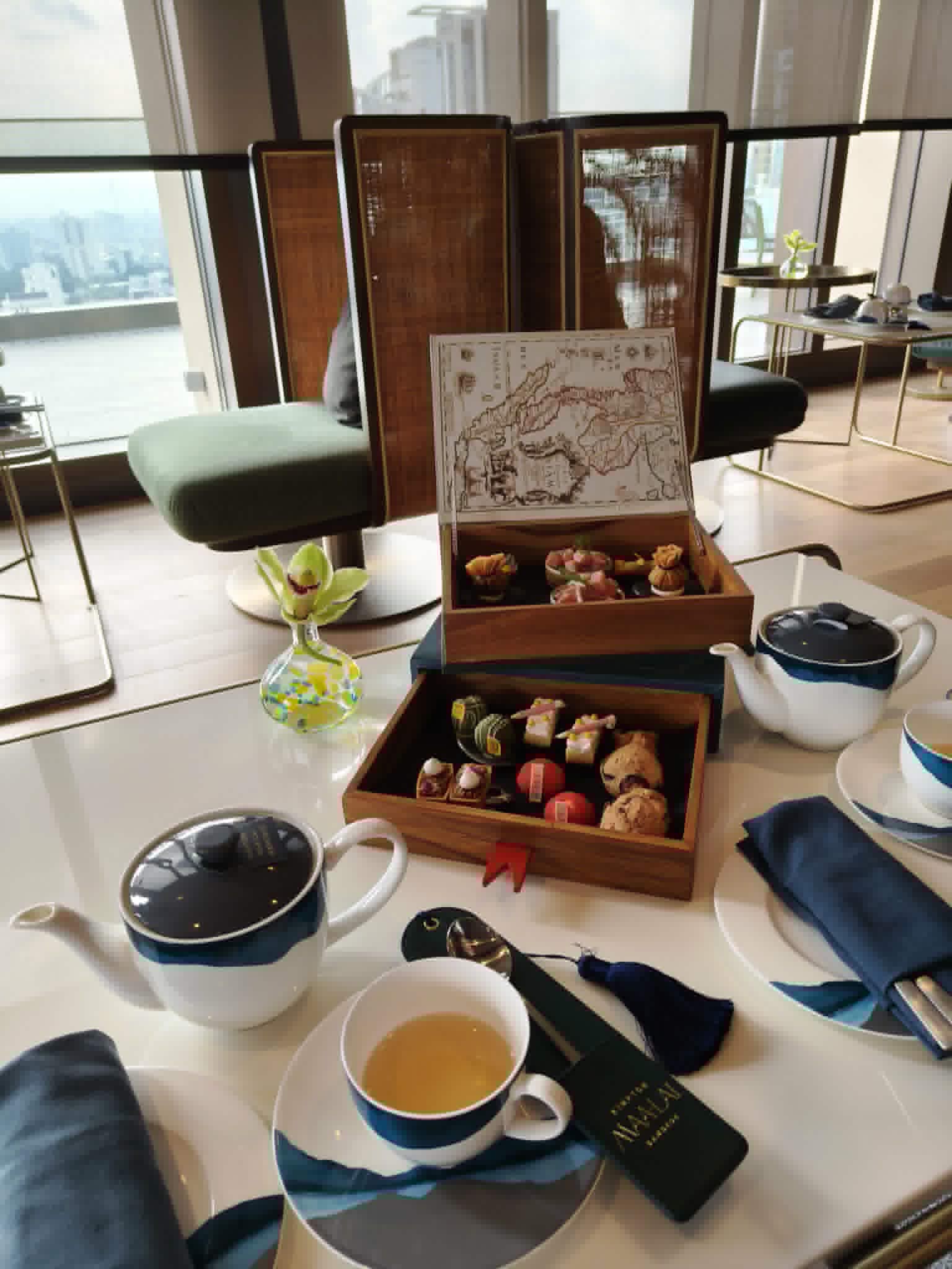 Tea set with a wooden box of pastries on a table with a cityscape view at Kimpton_Maa-Lai_Bangkok