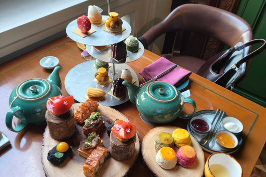 Tea set with pastries and tea accessories on a wooden table near a window at the house of Sathorn