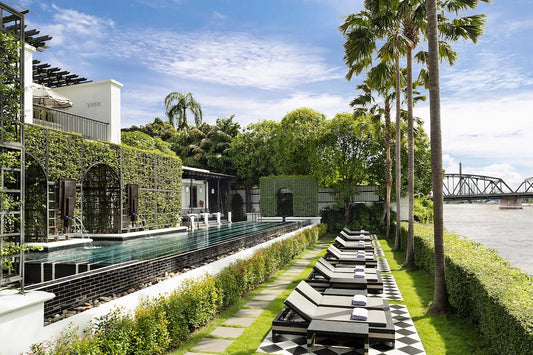 Outdoor pool area with lounge chairs, greenery, and a building in the background.