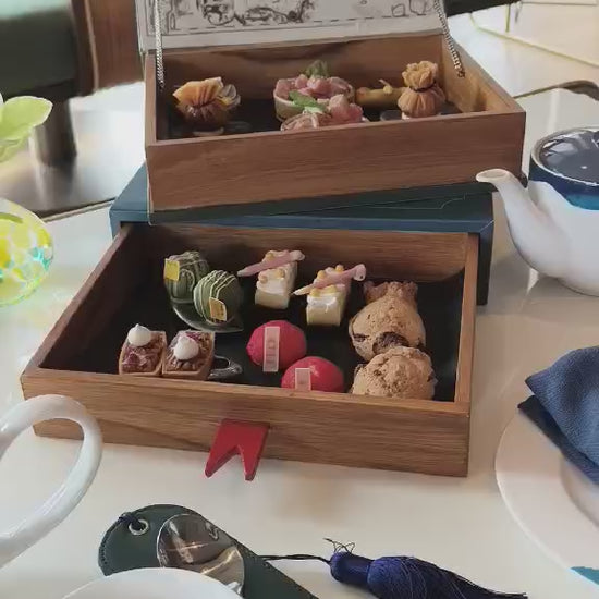Afternoon tea set in wooden boxes with pastries and tea at Maa-Lai Library Kimpton Bangkok
