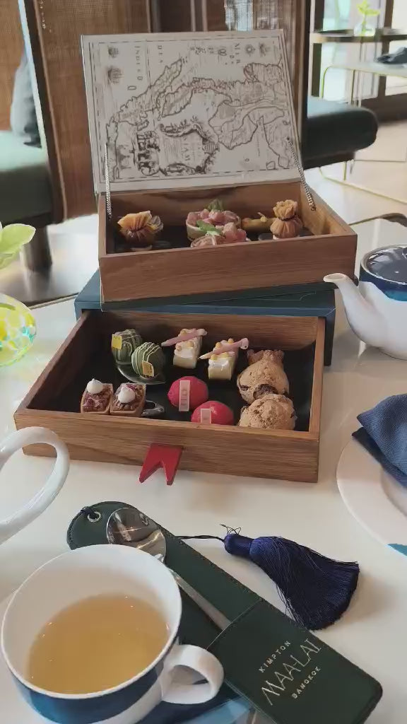 Afternoon tea set in wooden boxes with pastries and tea at Maa-Lai Library Kimpton Bangkok